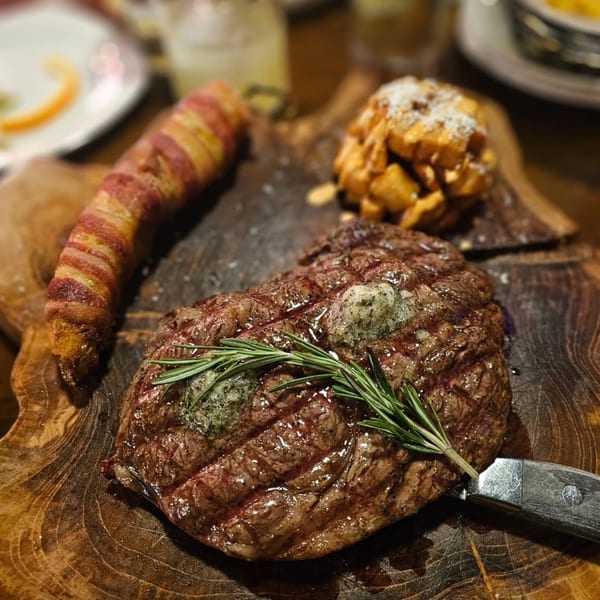 Grilled steak with rosemary and butter, bacon-wrapped plantain, and fried potatoes on a wooden board.