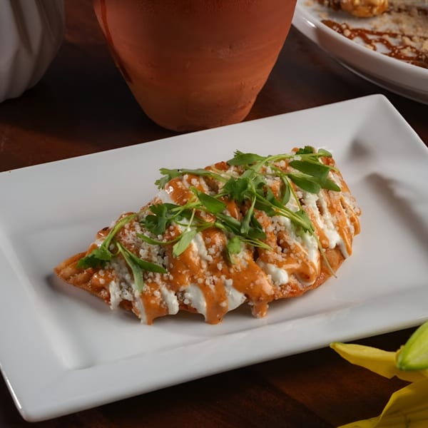 A Mexican empanada, drizzled with orange and white sauces, topped with cheese and cilantro.