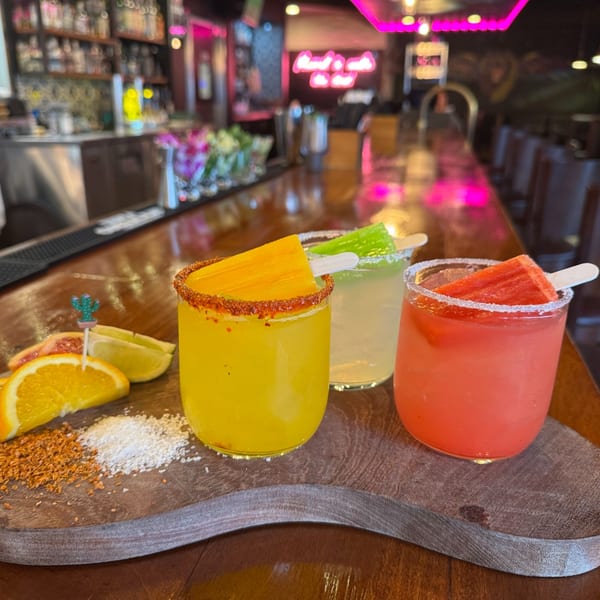 Three colorful Mezcal Mexican Restaurant margaritas with popsicles and citrus on a wooden tray at a bar.