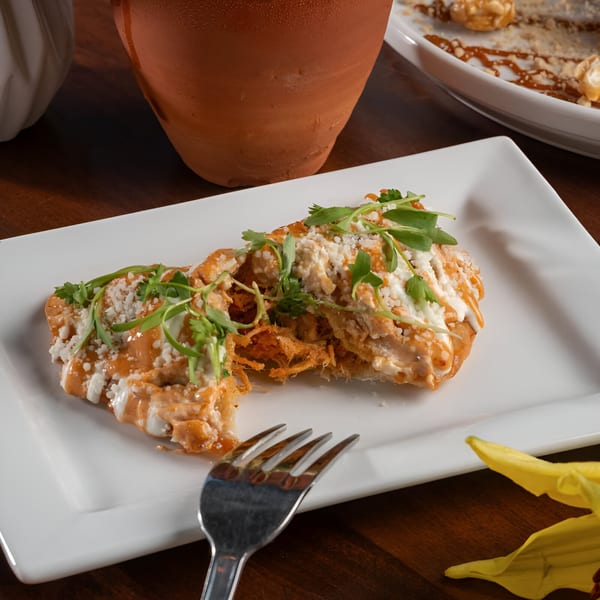 Two Mexican enchiladas topped with sauce, cheese, and cilantro on a white rectangular plate.