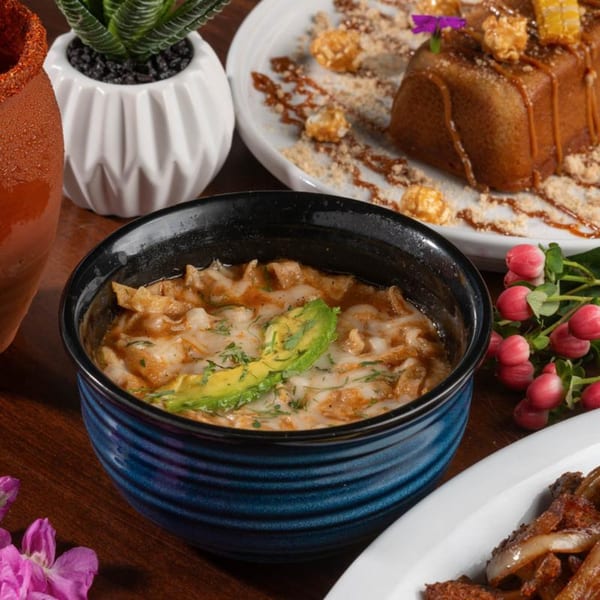 A blue bowl of Mexican tortilla soup with avocado and cilantro, next to a caramel dessert.
