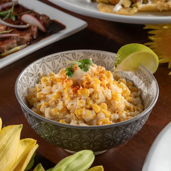 A bowl of Mexican street corn (Esquites) with a lime wedge, cilantro, and chili powder.